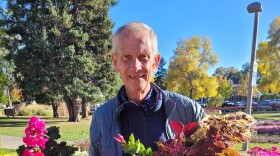 A man stands on a walkway holding several flowering plants.
